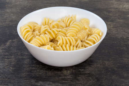 Boiled spiral pasta, also known as fusilli or rotini pasta in the small white bowl on a black surface, close-up in selective focusの写真素材