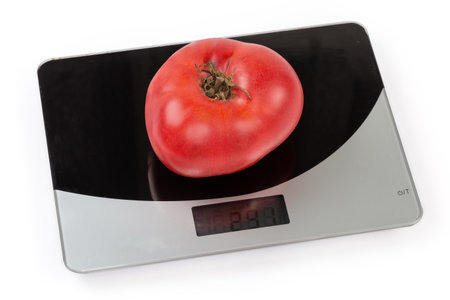 One whole big ripe pink tomato on the household digital kitchen scale on a white backgroundの写真素材