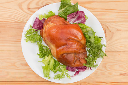 Pork boiled-smoked ham hock with different lettuce leaves on a white dish on the rustic table, top viewの写真素材