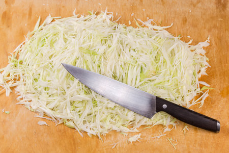 Heap of the shredded late white cabbage for preparing sauerkraut and kitchen knife on the large wooden cutting boardの写真素材