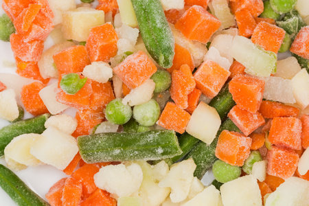 Mixture of the sliced frozen green beans, cauliflower, cubes of carrot, and green peas covered with rime, top view close-up, backgroundの写真素材