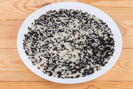 Mixture of the raw long-grained black and white rice on a white dish on the rustic tableの写真素材