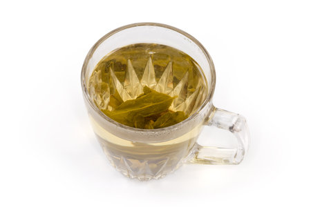 Freshly brewed green tea in the transparent glass cup with unfurled tea leaves at the bottom of the...