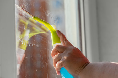 Domestic plastic scraper with inbuilt spray bottle for flat glass surfaces cleaning in hand during a...