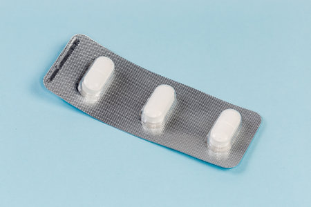 Small blister pack with three white pills of pharmaceutical product on a blue surface