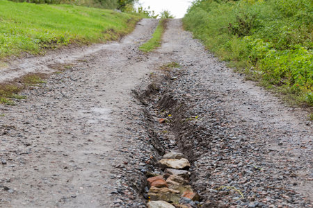 Washed out dirt road  covered with gravel on the hillside, with scour on the middle of the roadbed...