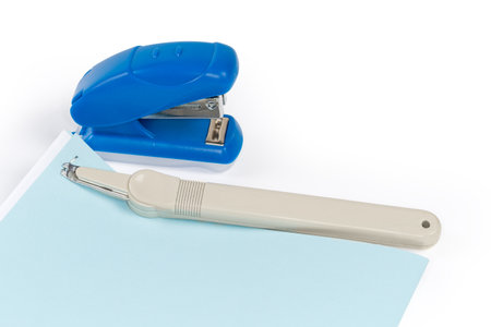 Simple pen type staple remover on the stapled blue and white sheets against the small manual paper stapler on a white backgroundの写真素材