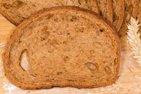 Slice of the dark brown bread made from rye and wheat flour among the ears and wheat grains on the...