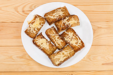 Hot open sandwiches made with small slices of brown grain bread and grated melted cheese on the white dish, top view on a rustic wooden tableの写真素材