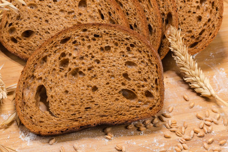 Slices of the dark brown bread made from rye and wheat flour among the ears and wheat grains on the...