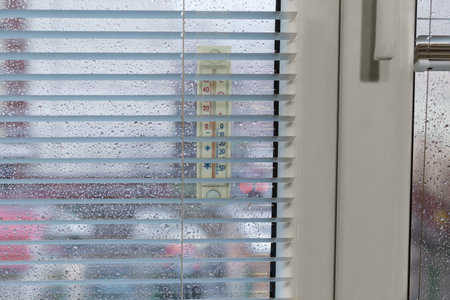 Part of the modern window with window panes covered with water drops, attached outdoor thermometer,...