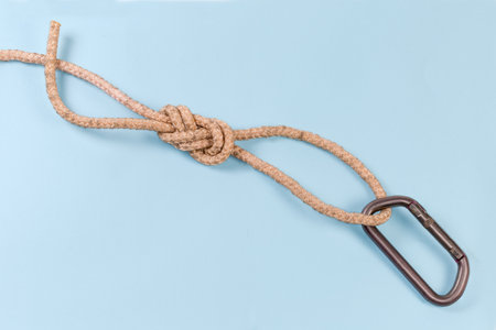 Oval titanium carabiner in rope knot as Ð°igure-eight loop, also known as Flemish loop on a blue backgroundの写真素材