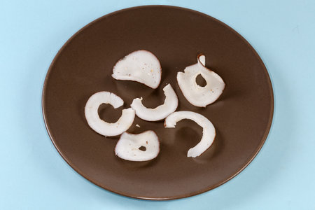 Dried slices of coconut flesh in the form of circles on brown dish on a blue backgroundの写真素材