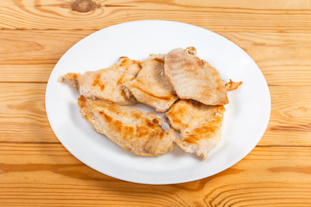 Cut to the flat slices grilled chicken breast on a white dish on the rustic tableの写真素材