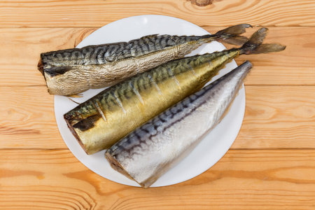 Whole hot-smoked, cold-smoked and salted Atlantic mackerel without heads on dish on the rustic tableの写真素材