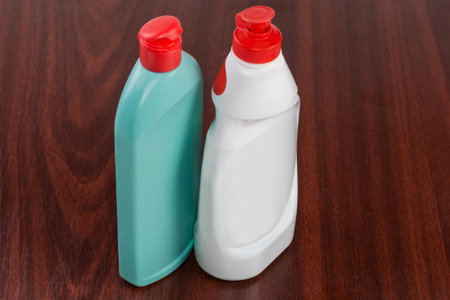 Blue-green and white plastic bottle of various household cleaning agent with not fully closed red...