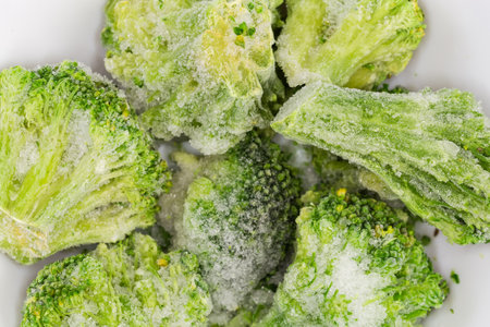 Branches of the frozen broccoli covered with rime in the small white bowl, fragment top view close-upの写真素材