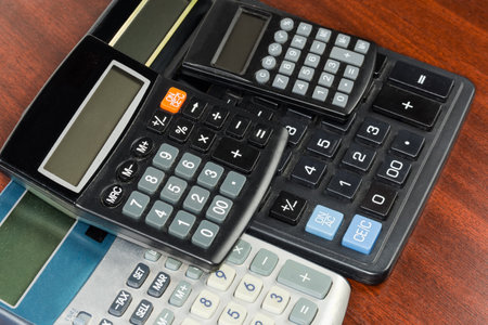 Various modern used electronic desk and pocket calculators different sizes with the liquid-crystal displays stacked on a red wooden table, fragment in selective focusの写真素材