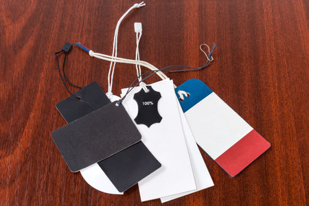 Blank carton clothing swing tags different forms and colors on the hanging ropes lie on the red wooden tableの写真素材