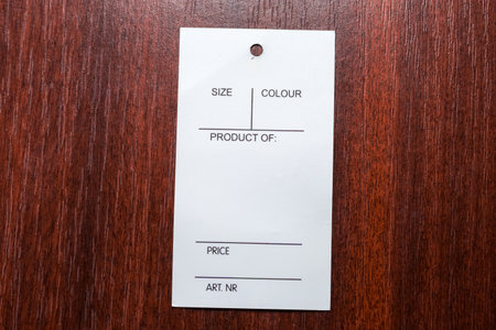 Blank white carton clothing swing tag in the form of the rectangular carton sheet with hole lies on the red wooden table, top viewの写真素材