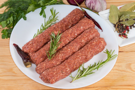 Several raw lula kebab on dish among the some vegetables, spices and greens on the rustic tableの写真素材