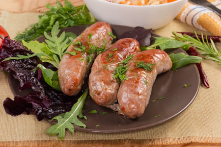 Baked thick short sausages with leaf vegetables on the brown dish, close-up in selective focusの写真素材