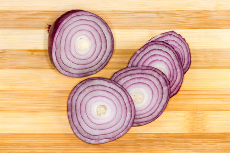 Bulb of the red onion partly cut into rings on a wooden bamboo cutting boardの写真素材