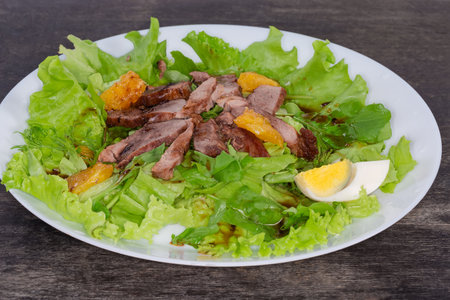 Salad made with boiled duck meat, egg, orange slices and different greens on a white dish on a black surface, close-up in selective focusの写真素材