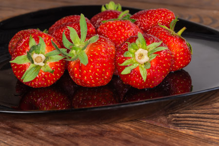 Washed garden strawberries with tails on the black dish, close-up in selective focusの写真素材