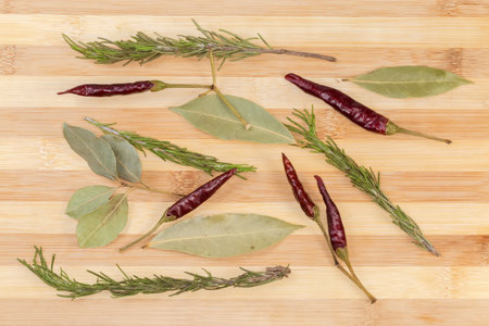Dried bay leaves, pods of red pepper chili and rosemary stems on a bamboo wooden surface, top viewの写真素材