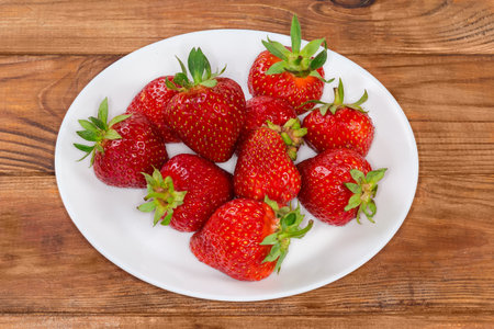 Washed garden strawberries with tails on the white dish on a rustic tableの写真素材
