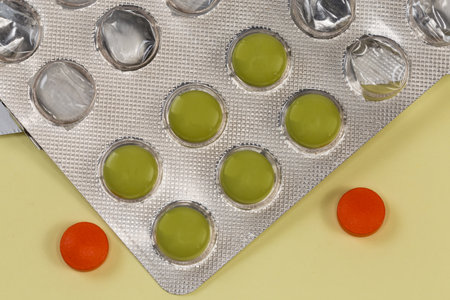 Green pills in partly used blister pack and two red pills separately on an yellow surface, top view