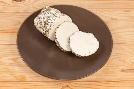 Pieces of soft cheese made with mixtures of various milk and slathered in different spices and herbs on a brown dish on a rustic tableの写真素材