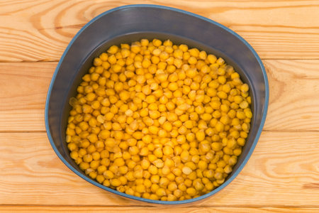 Whole uncooked yellow chickpeas soaked in cold water in the blue-gray bowl before preparing for faster cooking on the rustic table, top viewの写真素材