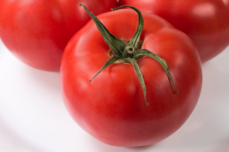 Whole big ripe pink tomatoes on the white dish, close-up in selective focusの写真素材