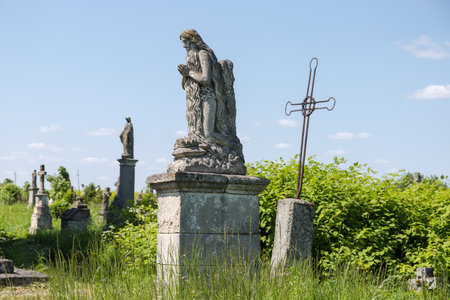 Ancient stone tombstone in the form of the praying Jesus sculpture on the old Christian cemetery against the other tombstones and sky in sunny dayの写真素材