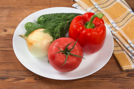 Different fresh vegetables and greens as ingredients for salad preparation on the white dish on the rustic tableの写真素材