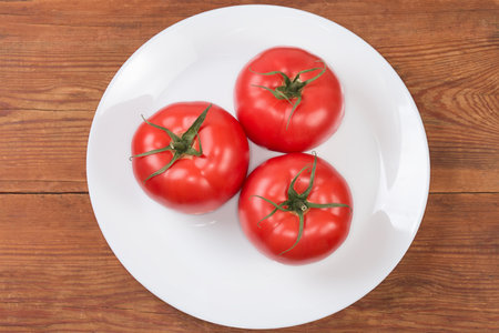 Whole big ripe pink tomatoes on the white dish on the rustic table, top viewの写真素材