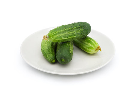 Freshly harvested green cucumbers on a white dish on a white backgroundの写真素材