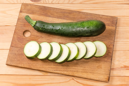 One whole and one sliced into circles dark green zucchini on the wooden cutting board on the rustic tableの写真素材