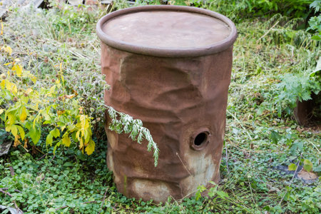 Old rusty iron barrel with lateral fill hole and uneven walls with dents stand outdoors among the grassの写真素材
