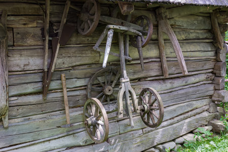 Old partly broken undercarriage of the wooden four-wheeled horse-drawn rural wagon hangs on the wall of the ancient wooden buildingの写真素材