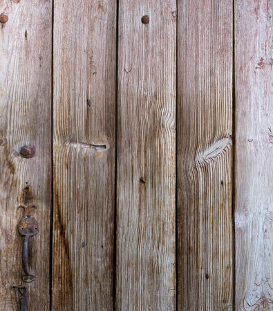 Fragment of the old wooden door made with roughly handled planks with knots and iron wrought iron door handleの写真素材