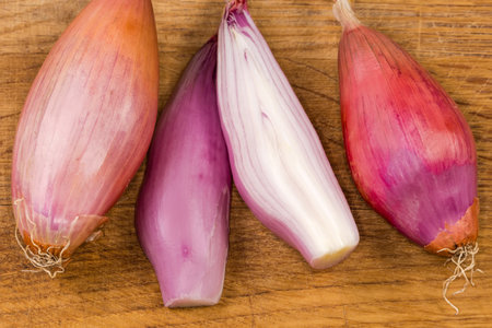 Whole and halves of the oblong oval bulbs of the red onion of variety shallot on the old wooden cutting board, top view close-upの写真素材