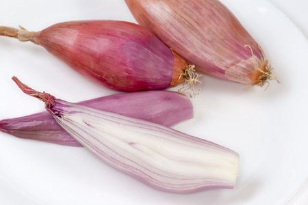 Whole and halves of the oblong oval bulbs of the red onion of variety shallot on the white dish close-upの写真素材
