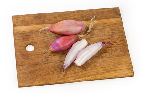 Whole and halves of the oblong oval bulbs of the red onion of variety shallot on the wooden cutting board on a white backgroundの写真素材