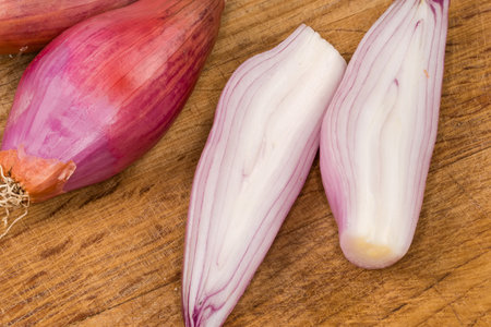Whole and halves of the oblong oval bulbs of the red onion of variety shallot on the old wooden cutting board, top view close-upの写真素材
