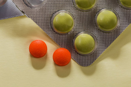 Green pills in partly used blister pack and two red pills separately on an yellow surface, top view close-upの写真素材
