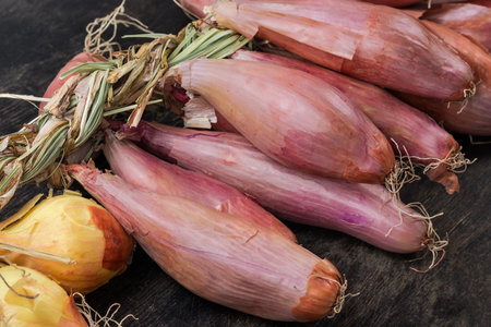 Bundle of freshly harvested red shallot and common onions bulbs braided in a row lies on the black surface, fragment close-upの写真素材