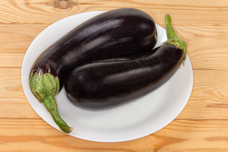 Two freshly harvested ripe whole purple eggplants on dish on the wooden rustic tableの写真素材